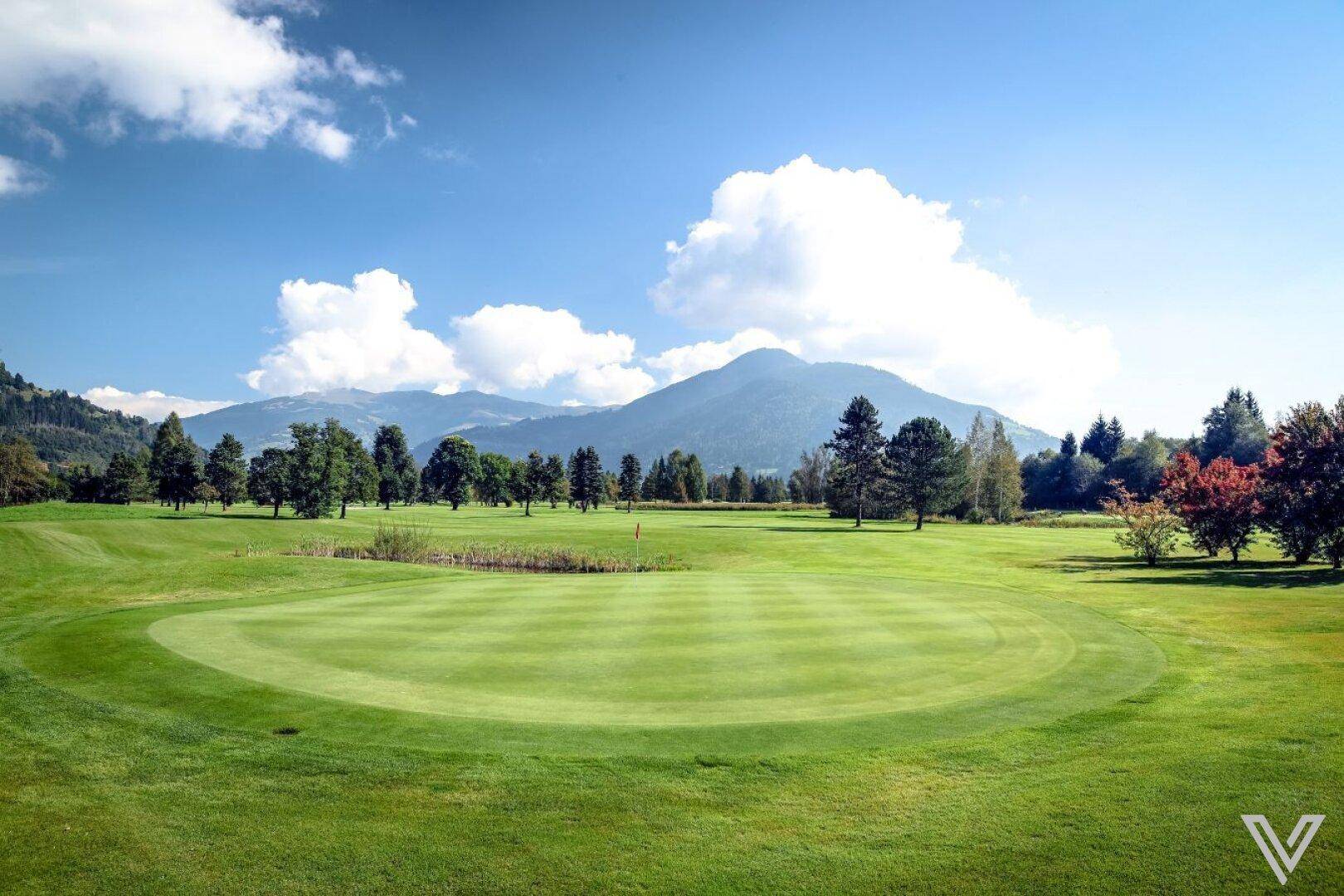 Weitläufiger Golfplatz mit gepflegtem Grün und majestätischer Bergkulisse unter blauem Himmel.