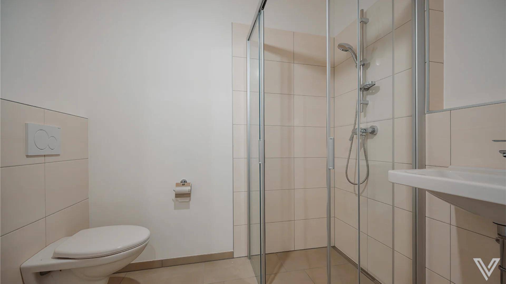 Helles Badezimmer mit Duschkabine, Wand-WC und beigefarbenen Fliesen.