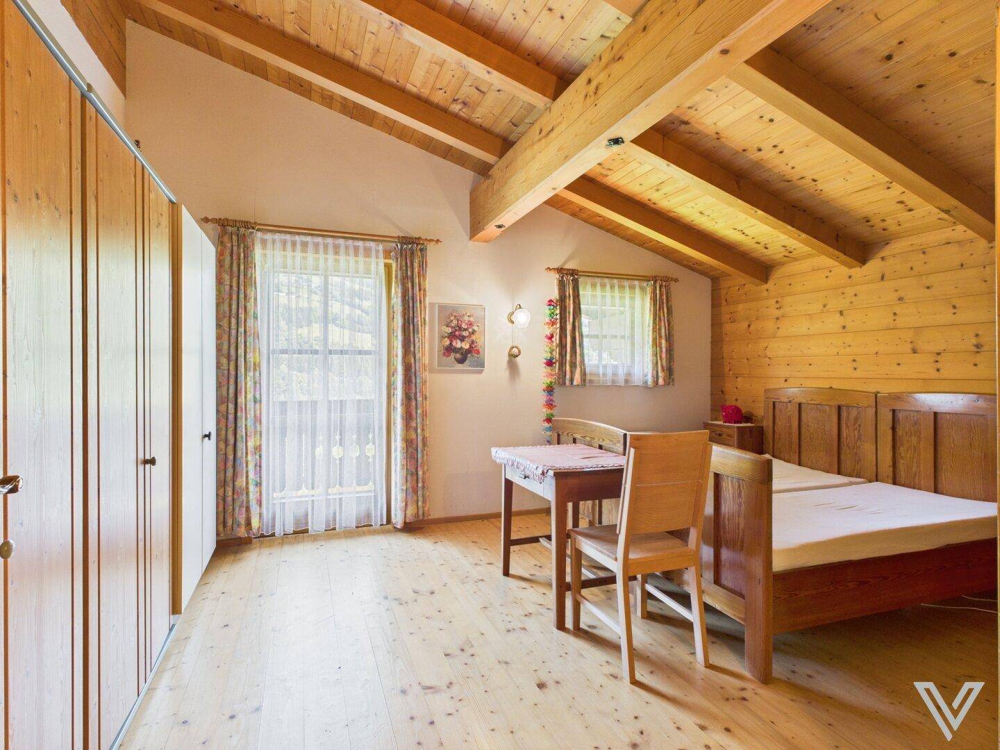 Helles Schlafzimmer mit Holzbalkendecke, Holzboden und traditionellen Holzmöbeln.