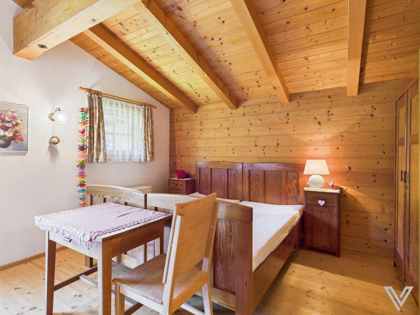 Gemütliches Schlafzimmer mit Holzbalkendecke, Doppelbett und rustikalen Holzmöbeln.