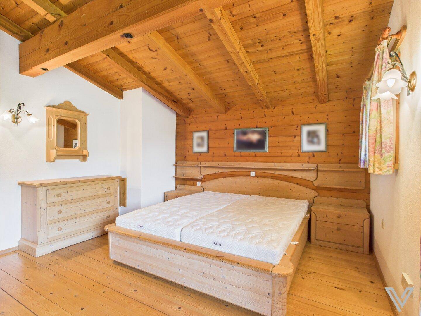 Geräumiges Schlafzimmer mit Doppelbett, Holzbalkendecke und passenden Holzmöbeln.