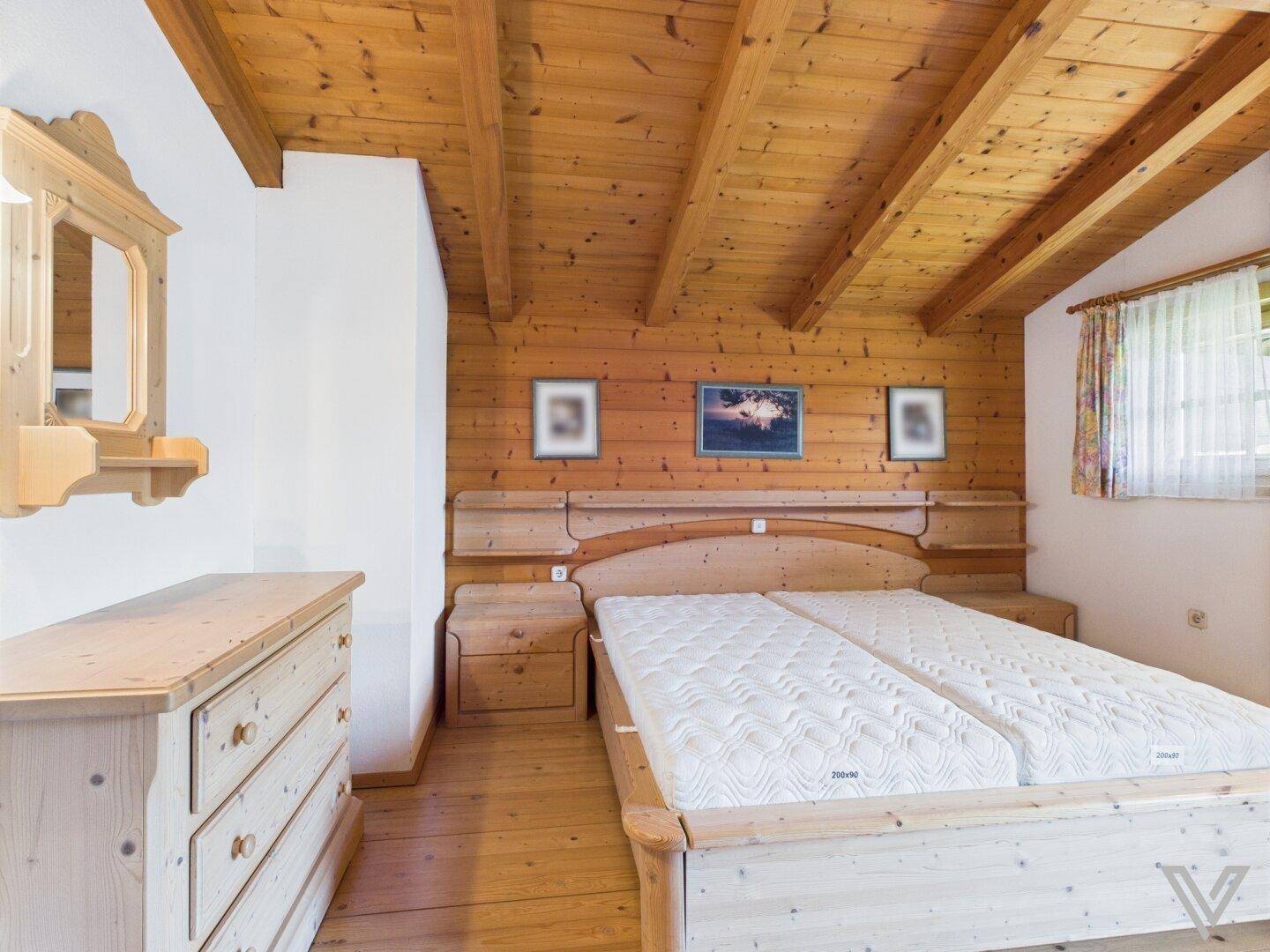 Helles Schlafzimmer mit Doppelbett, Holzbalkendecke und rustikaler Kommode.