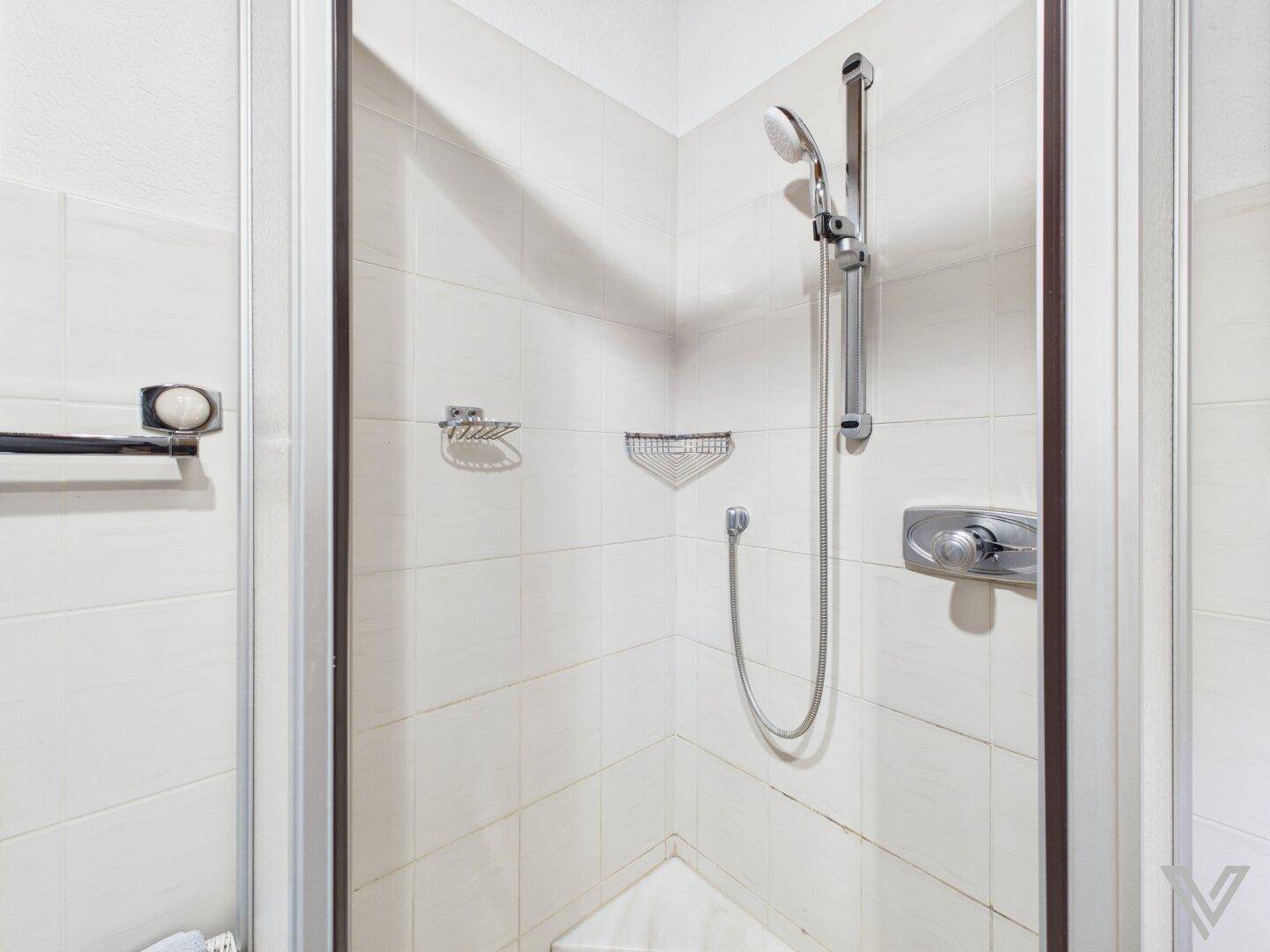 Duschkabine mit weißen Fliesen und einfacher Ausstattung im Badezimmer.