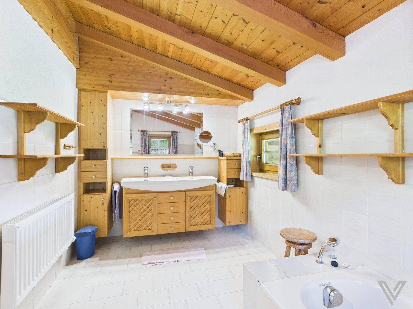 Geräumiges Badezimmer mit Doppelwaschbecken, Badewanne und Holzbalkendecke.