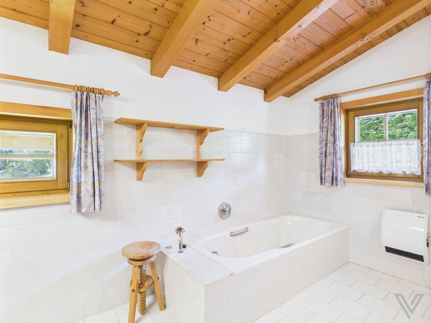 Badezimmer mit Badewanne, gefliesten Wänden und Holzbalkendecke.