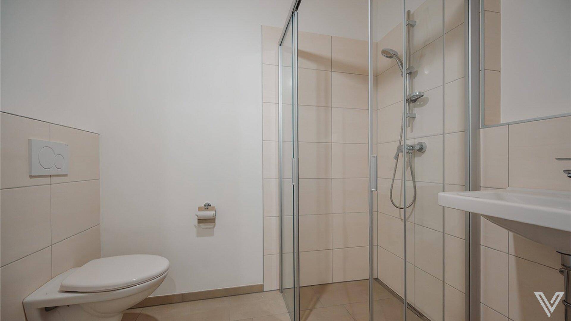 Funktionales Badezimmer mit Duschkabine, wandhängendem WC und Waschbecken in hellen Fliesen.