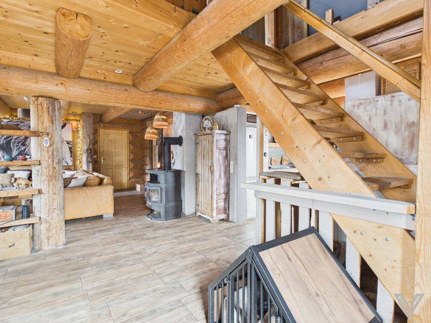 Offener Wohnbereich mit Holztreppe, Kaminofen und rustikalem Charme des Blockhauses.