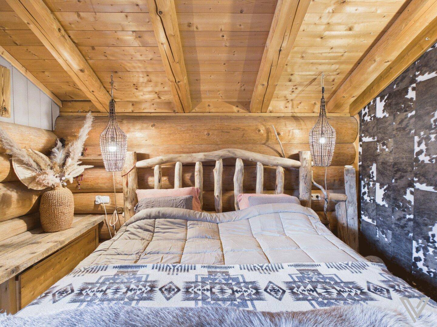 Gemütliches Schlafzimmer mit Holzbalken, rustikalem Bett und dekorativer Kuhfell-Tapete.