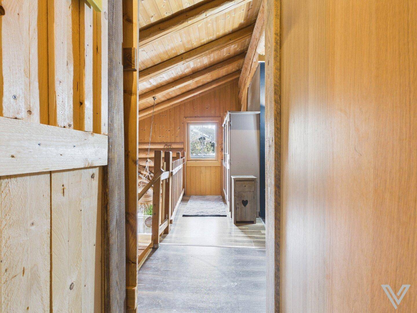 Heller Flur im Dachgeschoss mit Holzboden und Blick ins Grüne durch das Fenster.