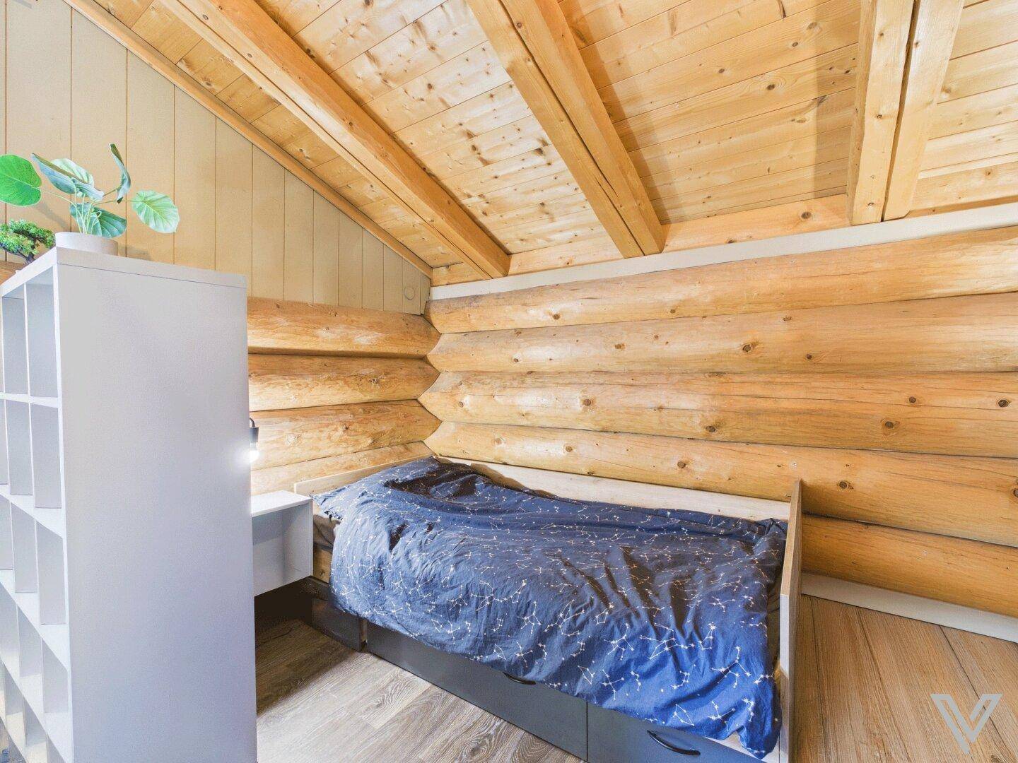 Kleines Schlafzimmer im Dachgeschoss mit Holzwänden und Einzelbett unter der Schräge.