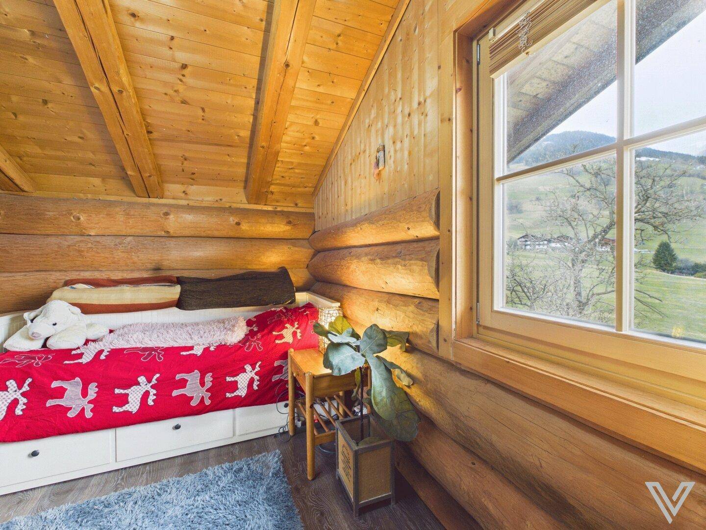 Helles Schlafzimmer im Dachgeschoss mit Holzwänden, Einzelbett und Bergblick.