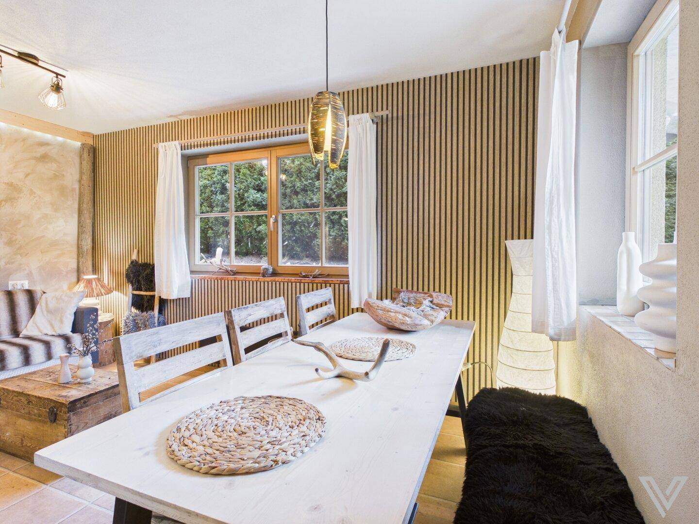 Essbereich mit Holztisch, Stühlen und vertikalen Holzpaneelen an der Wand mit Gartenblick.