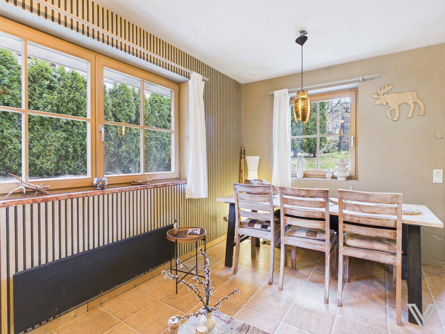 Essbereich mit Holztisch, Stühlen und Blick auf den grünen Garten durch das Fenster.