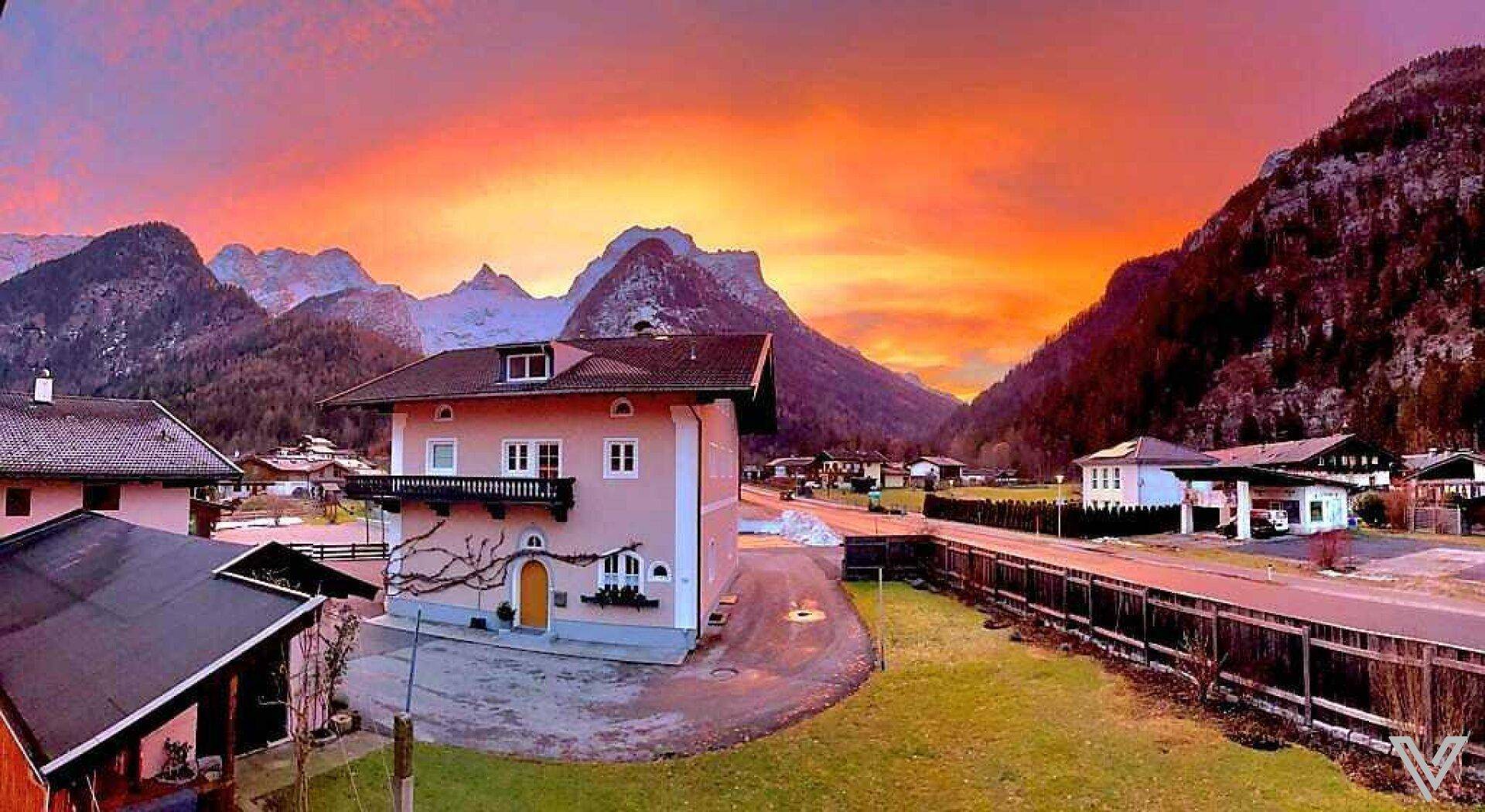 Hausfassade mit Balkon vor einer beeindruckenden Bergkulisse bei Sonnenuntergang.