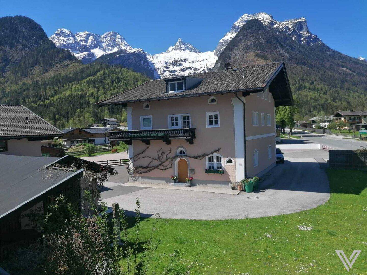 Hausfassade mit Balkon vor einer beeindruckenden Bergkulisse im Frühling oder Sommer.