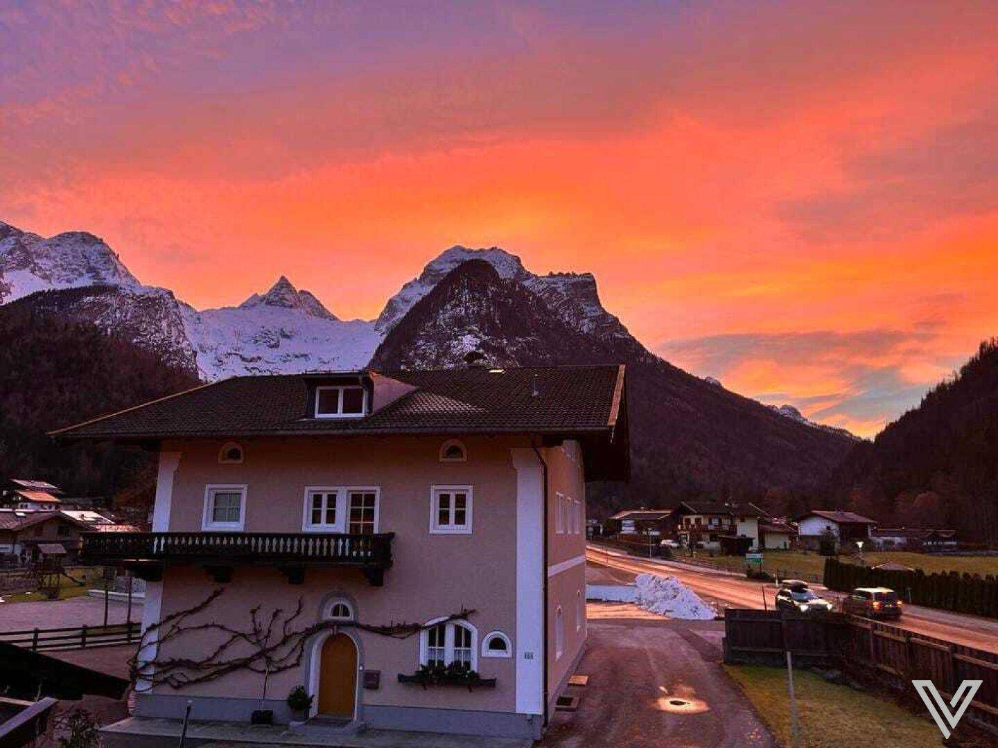 Ansicht des Hauses mit Balkon und verschneiten Bergen im Hintergrund während eines farbenprächtigen Sonnenuntergangs.