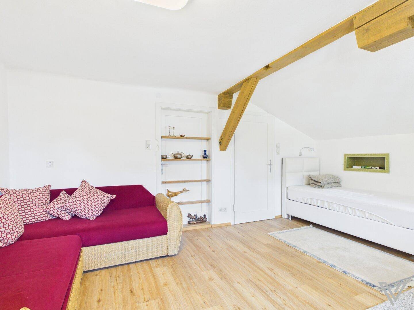 Schlafzimmer mit Sofa, Einzelbett, sichtbarem Holzbalken und Dachschräge.