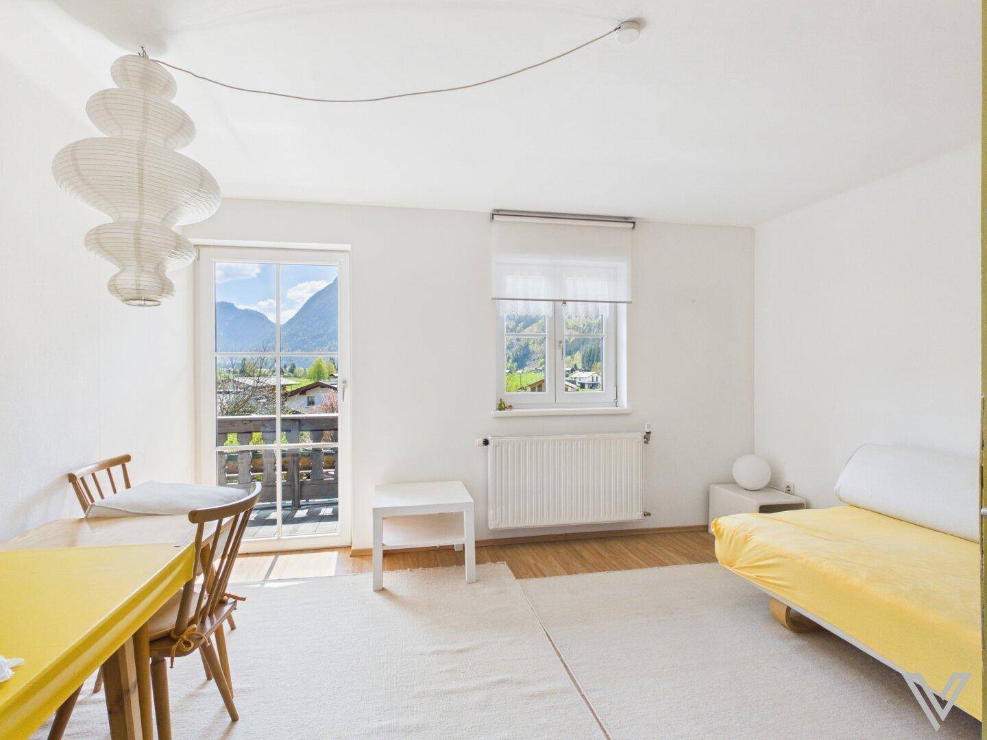Helles Zimmer mit gelbem Tisch, Tagesbett und Balkonzugang mit Bergblick.