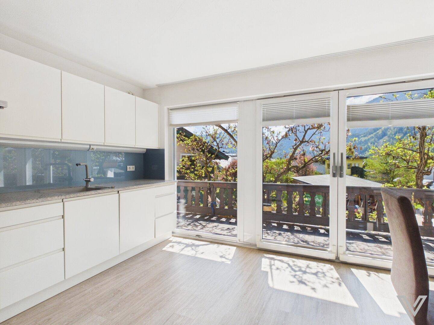 Helle Küche mit weißen Schränken, Granitarbeitsplatte und Zugang zu einem Balkon mit Bergblick.