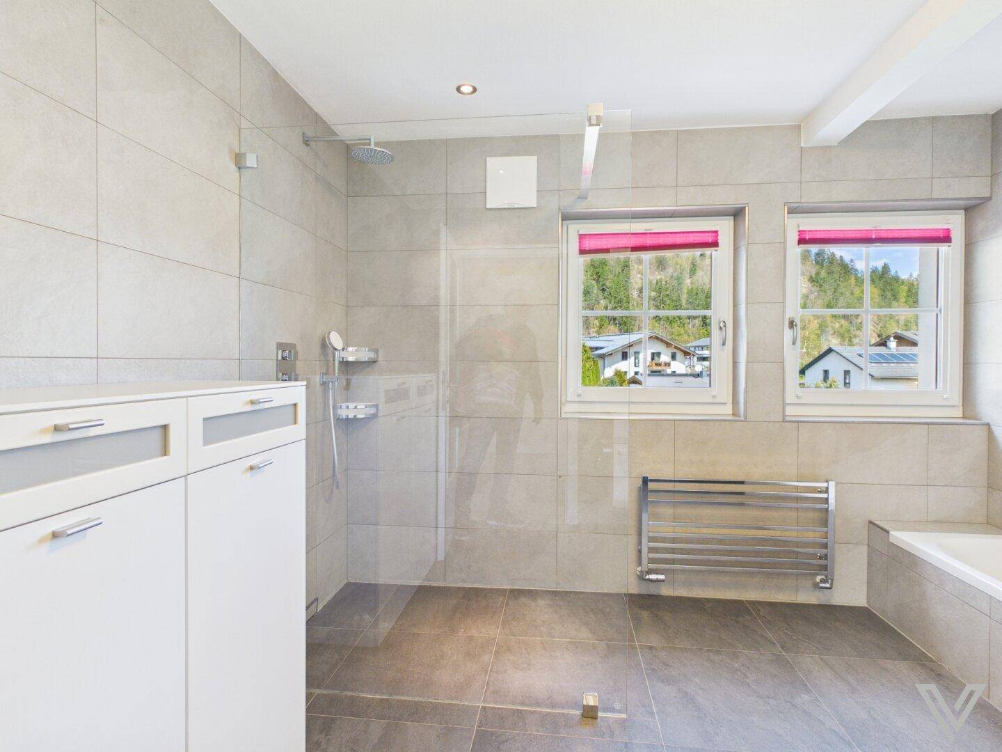 Modernes Badezimmer mit ebenerdiger Dusche, weißen Schränken und Fenstern mit Blick ins Grüne.