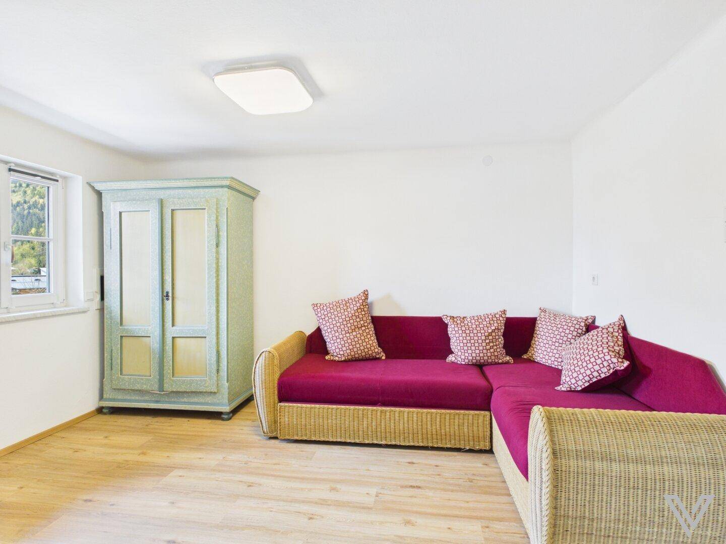 Gemütliches Schlafzimmer mit rotem Sofa, traditionellem Kleiderschrank und hellem Laminatboden.