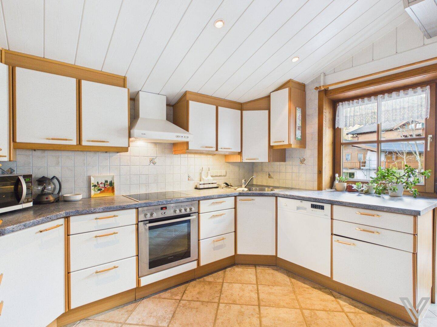 Traditionelle Küche mit hellen Holz- und weißen Schränken, Fliesenboden und Fenster.