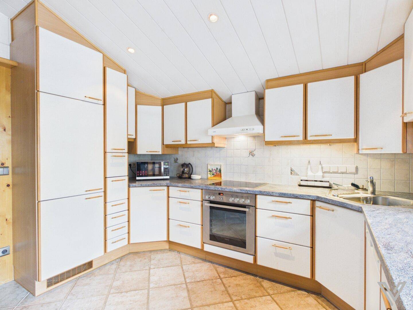 Voll ausgestattete traditionelle Küche mit Holz- und weißen Fronten sowie Fliesenboden.