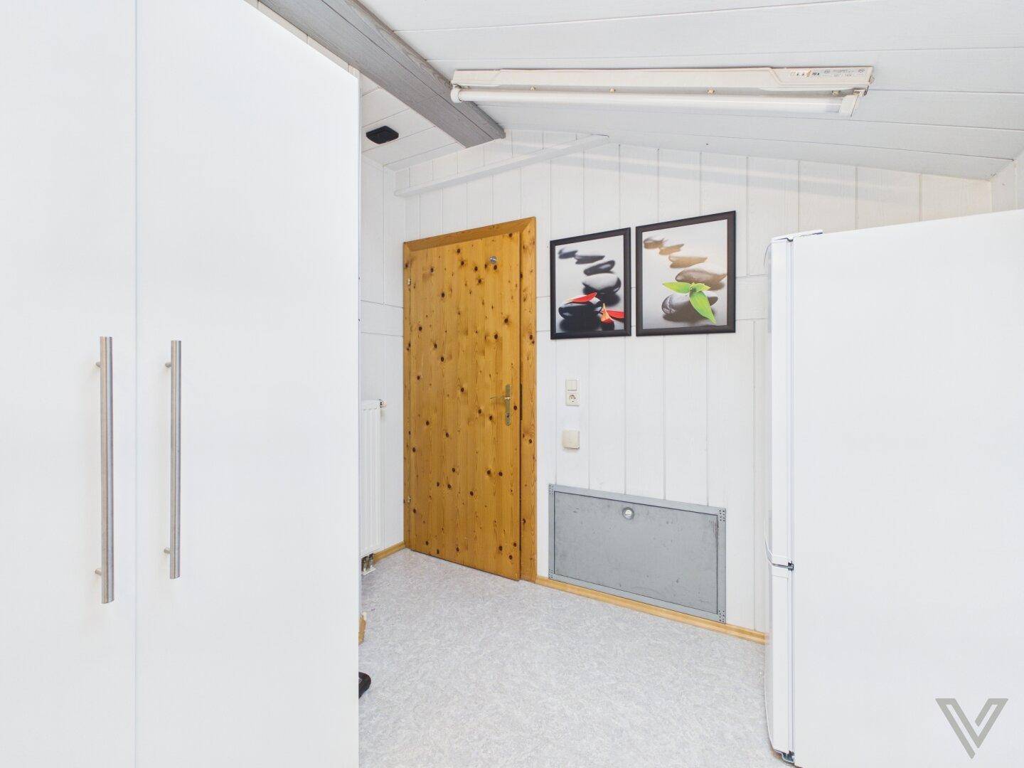 Praktischer Abstellraum mit weißem Schrank, Kühlschrank und Holztür.