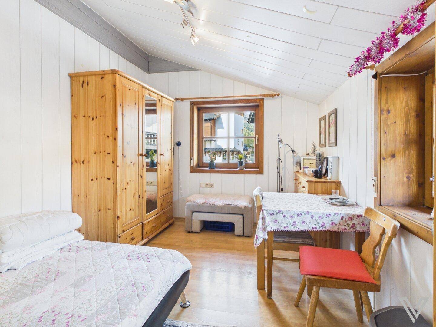 Helles Schlafzimmer mit Holzboden, Kleiderschrank und kleinem Esstisch.