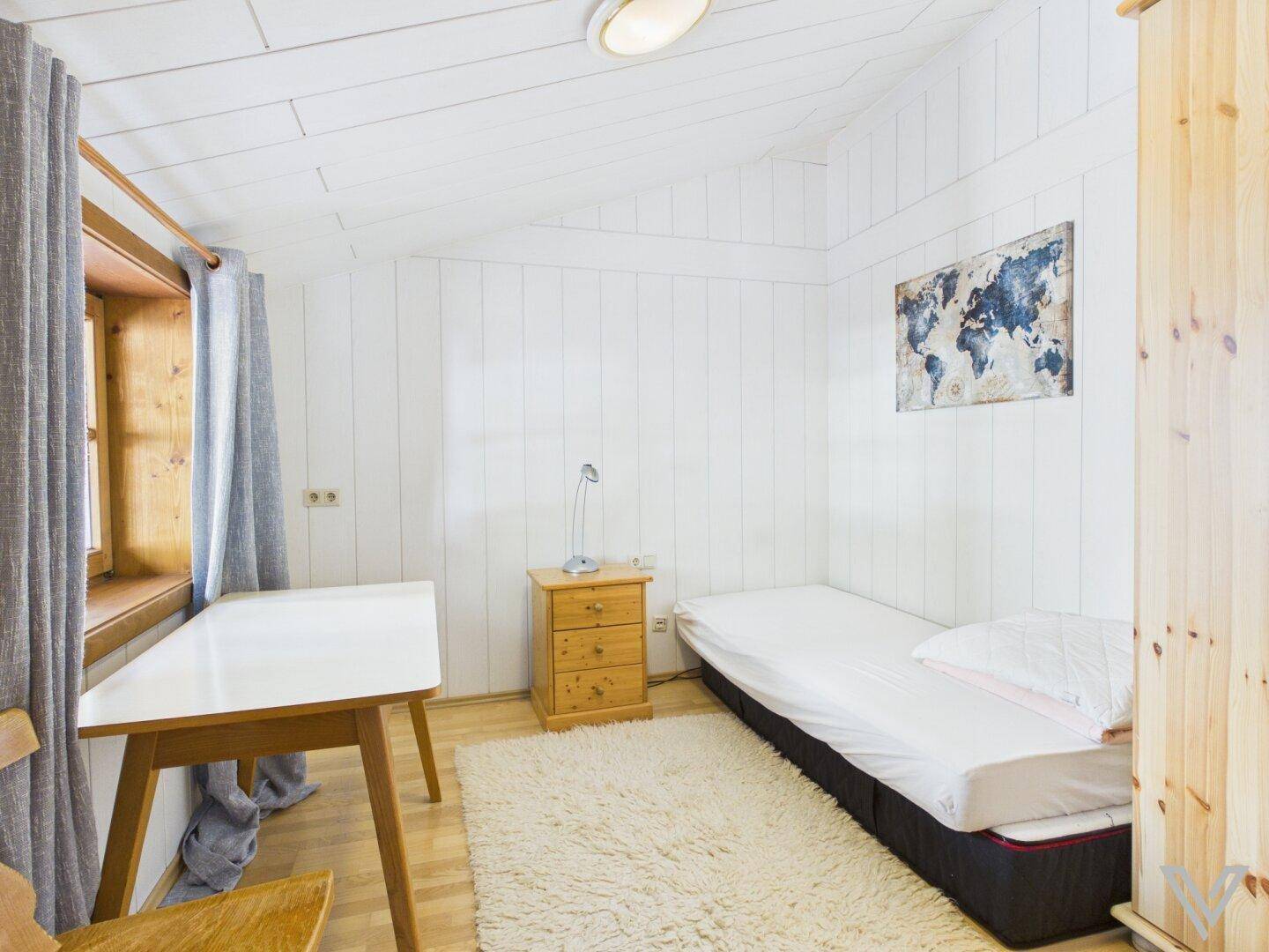 Kleines Schlafzimmer mit Einzelbett, Schreibtisch und Teppichboden.