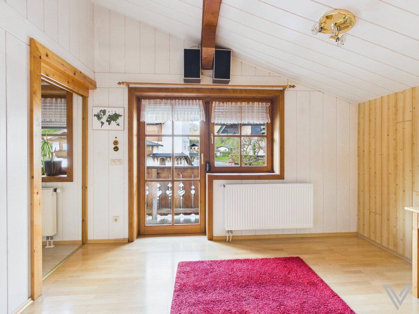 Helles Wohnzimmer mit Holztäfelung, Fenster und Zugang zu einem Balkon oder einer Terrasse.