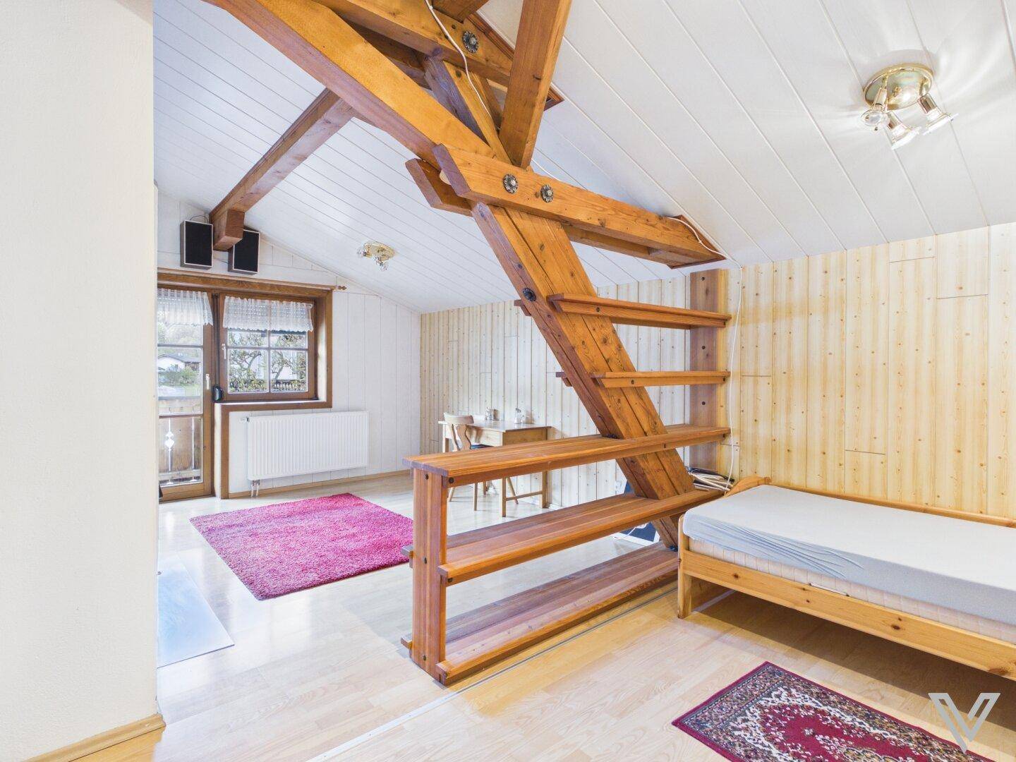 Gemütliches Schlafzimmer im Dachgeschoss mit sichtbaren Holzbalken und hellem Holzboden.