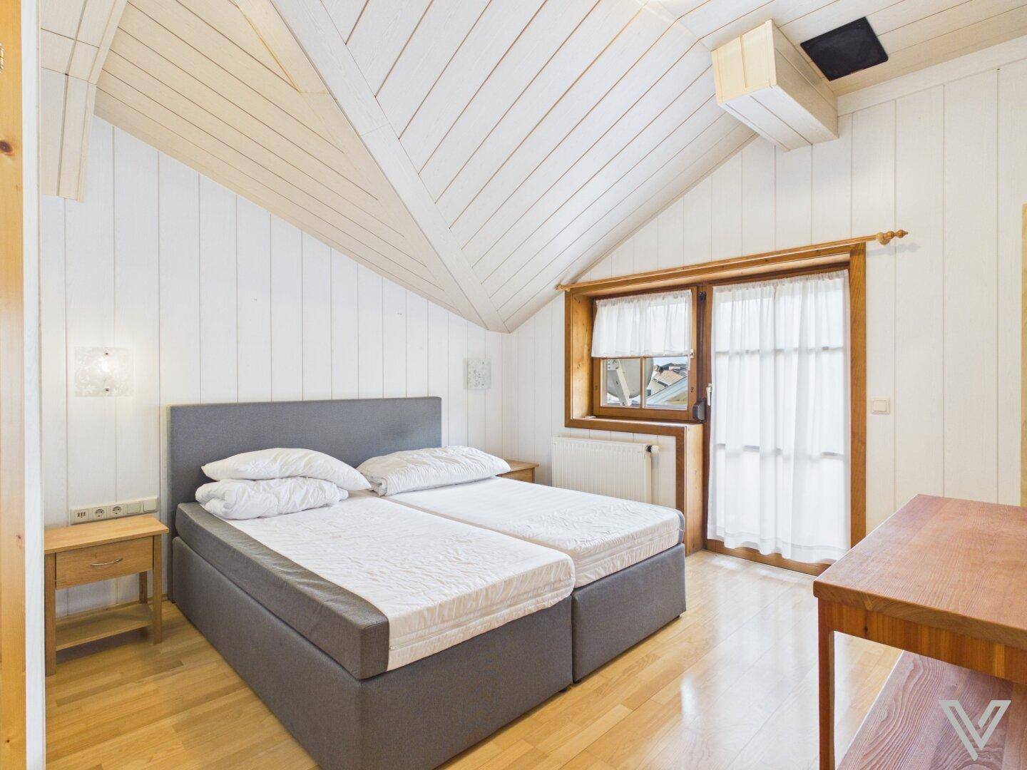 Helles Schlafzimmer im Dachgeschoss mit Doppelbett, Holzwänden und schrägen Decken.