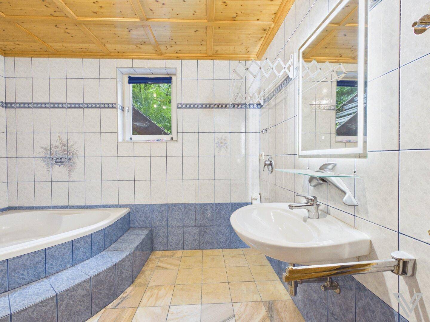 Badezimmer mit blauen und weißen Fliesen, Badewanne und Holzdecke.