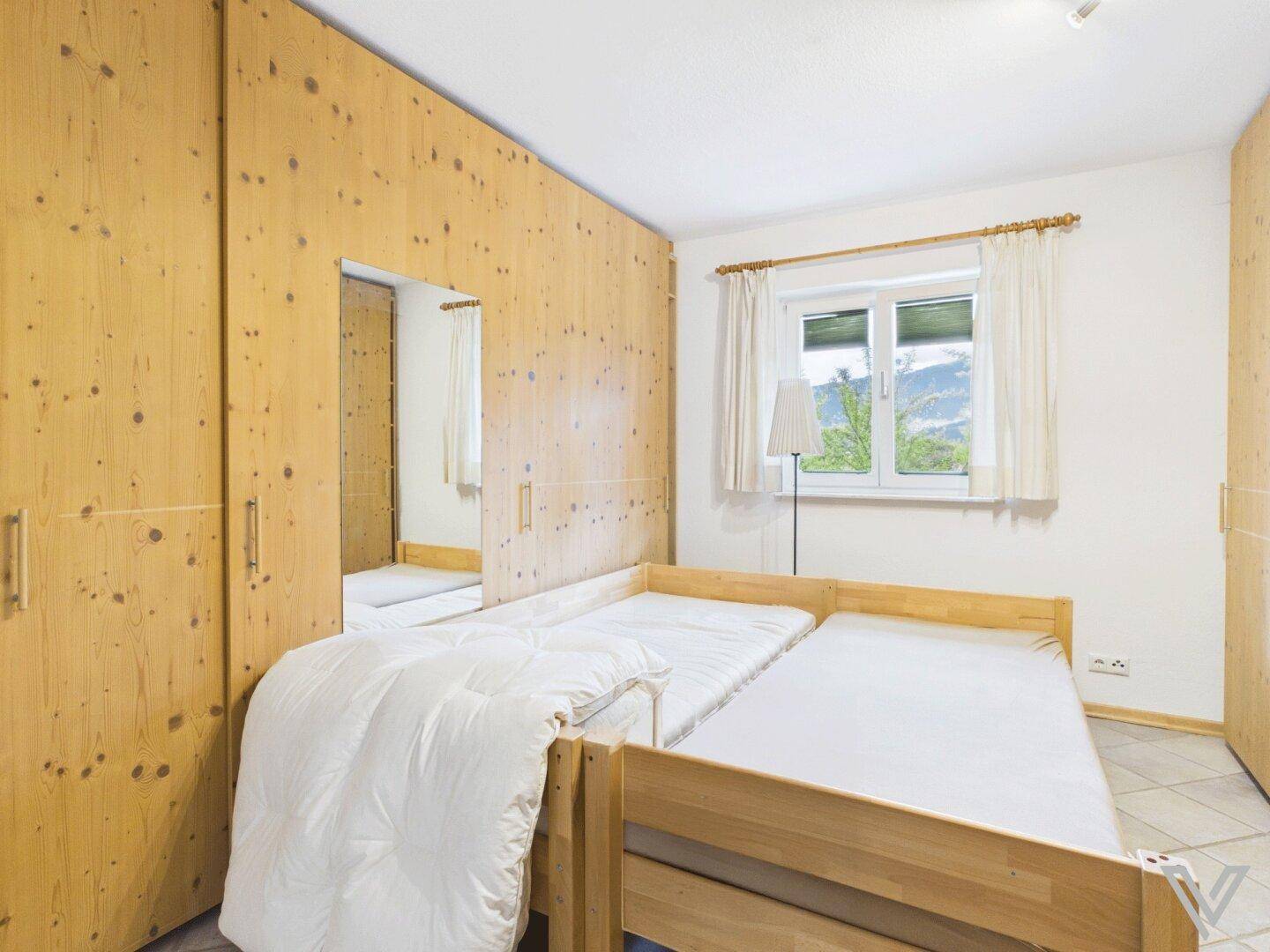 Schlafzimmer mit Holzschränken, Einzelbetten und Fenster mit Bergblick.