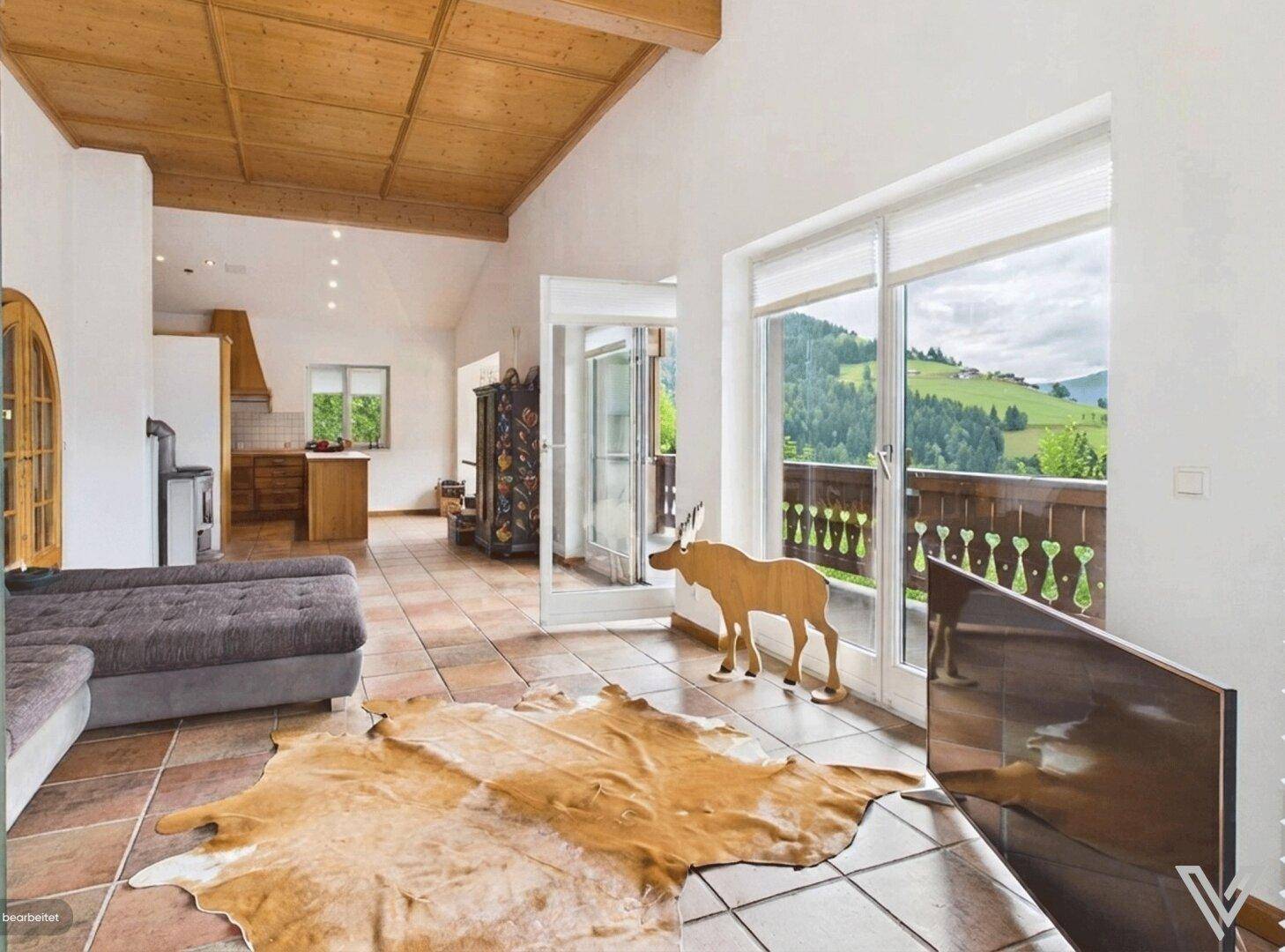 Heller Wohnbereich mit großen Fenstern, Bergblick und Zugang zum Balkon.