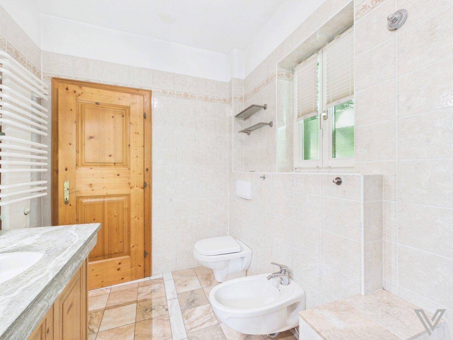 Helles Badezimmer mit Fliesenboden, WC, Bidet und beheiztem Handtuchhalter.