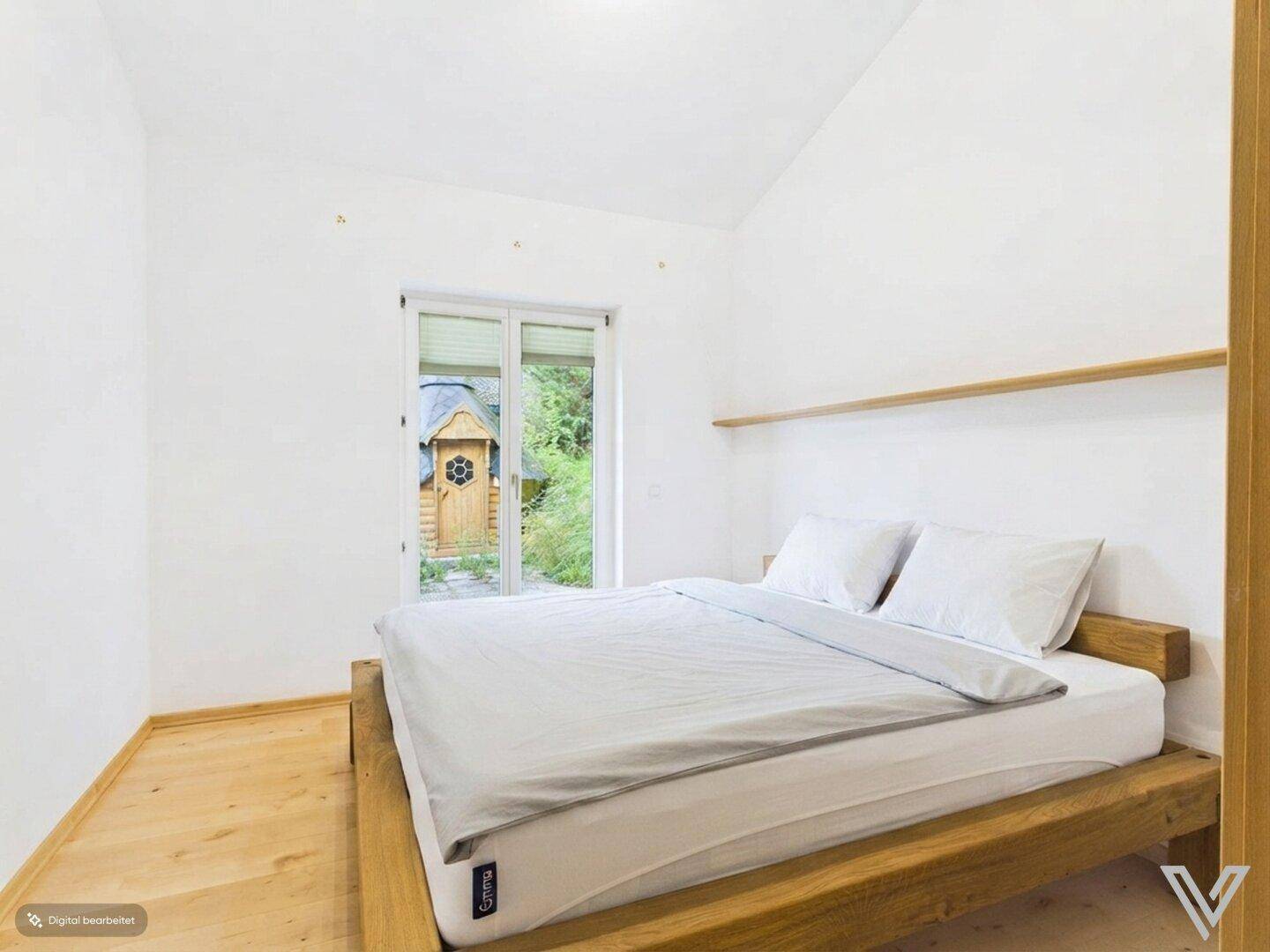 Schlafzimmer mit Holzbett, Parkettboden und Zugang zum Gartenbereich.
