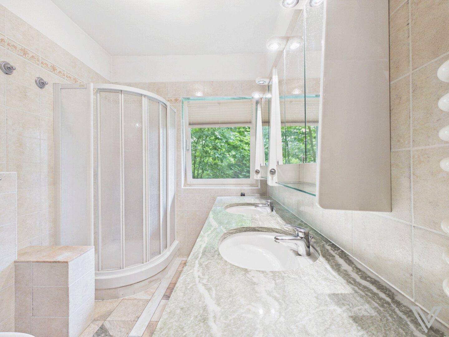 Badezimmer mit Doppelwaschbecken, Duschkabine und Fenster mit Blick ins Grüne.