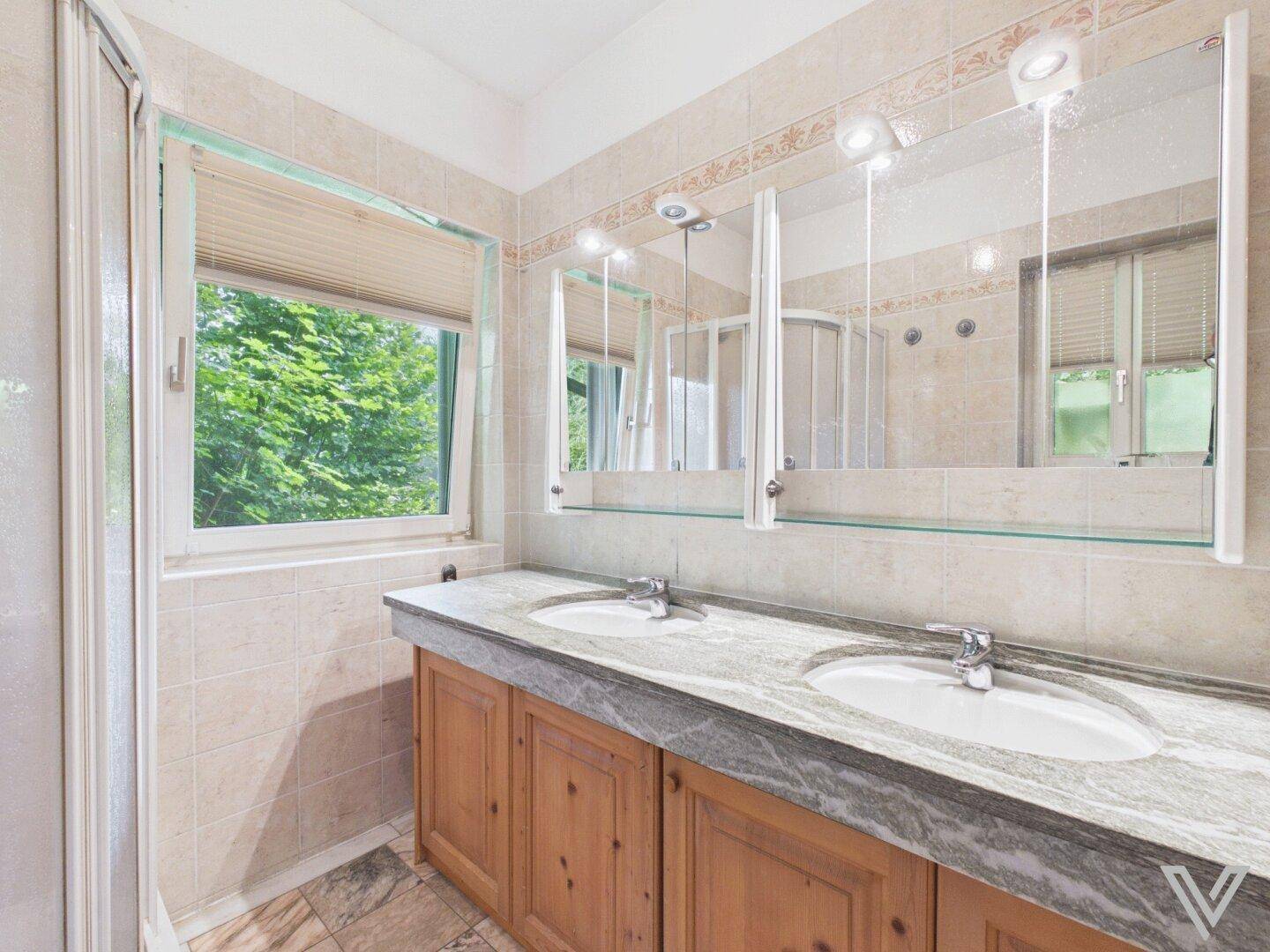 Badezimmer mit Doppelwaschbecken, Marmorplatte und Spiegelschrank.