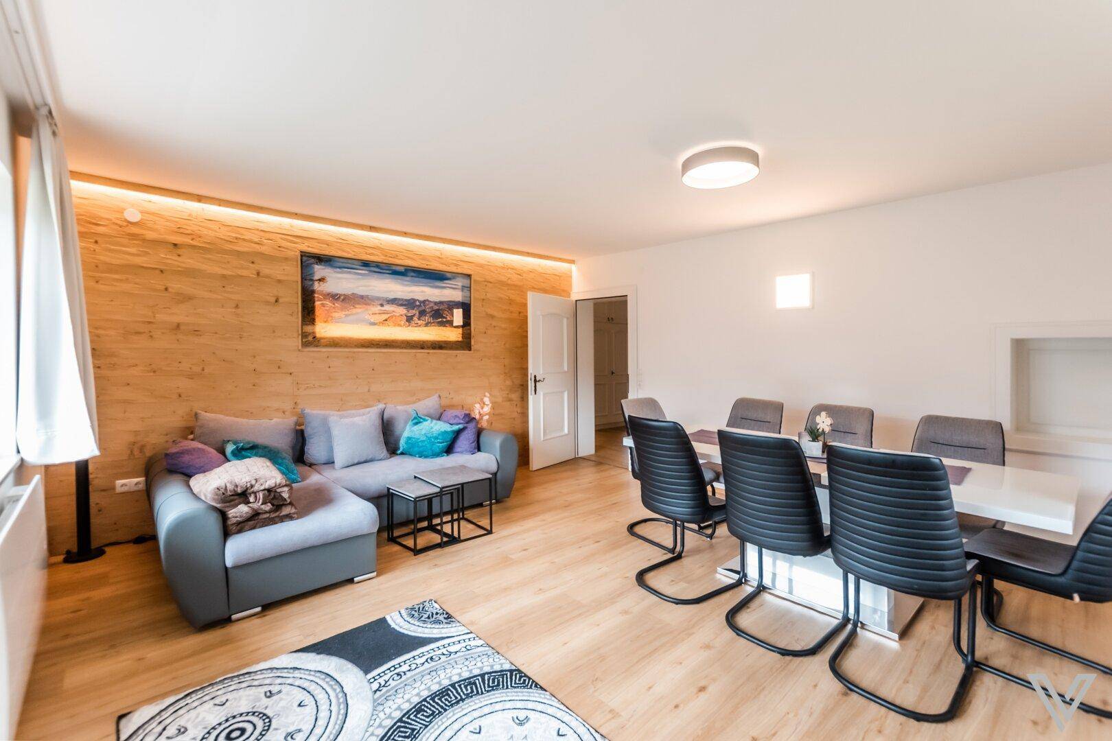 Geräumiger Wohn-Essbereich mit Holzwand, Sofa und großem Esstisch für gesellige Runden.