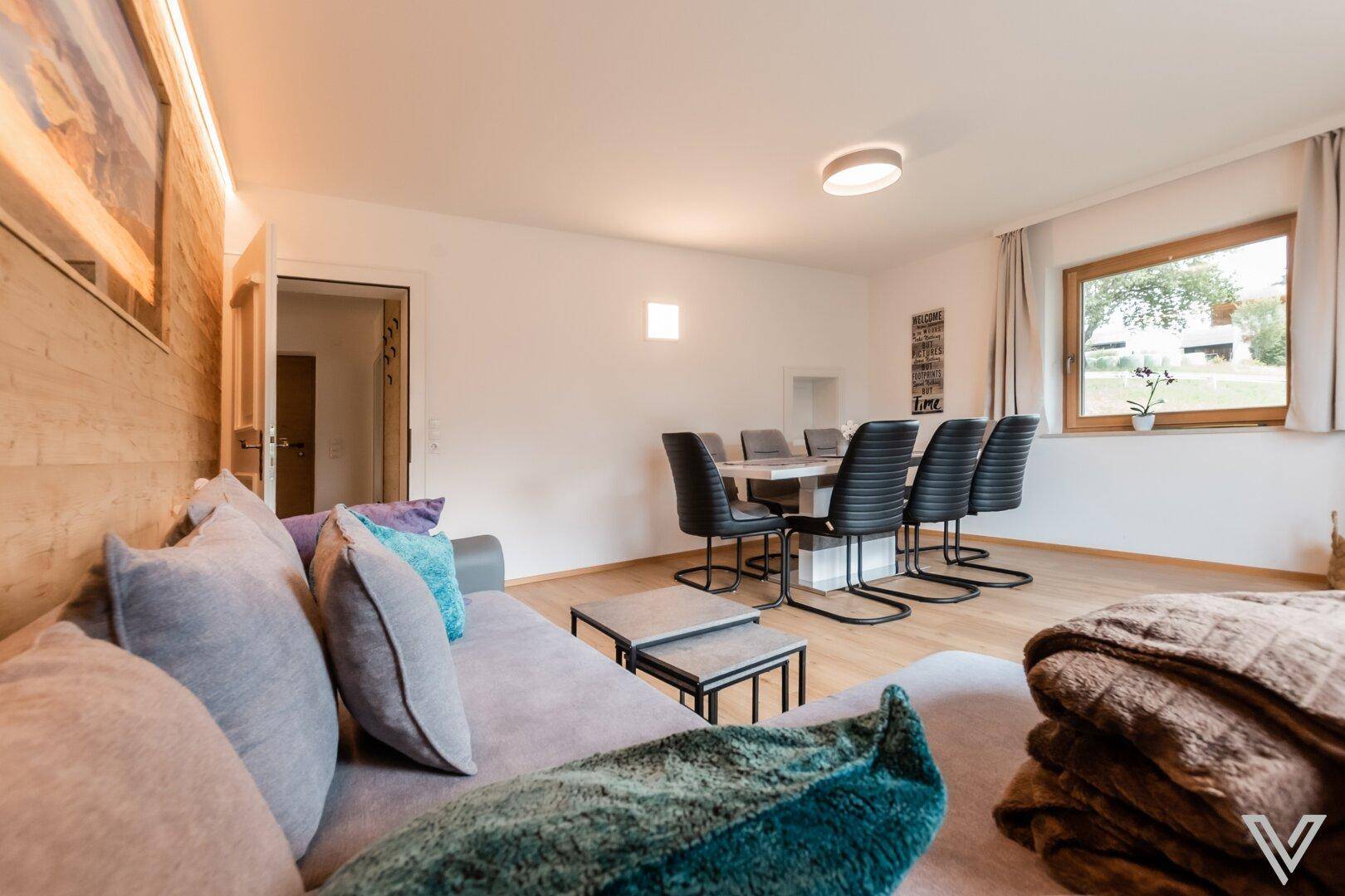 Gemütlicher Wohn-Essbereich mit bequemer Couch, Holzwand und Essgruppe für die ganze Familie.