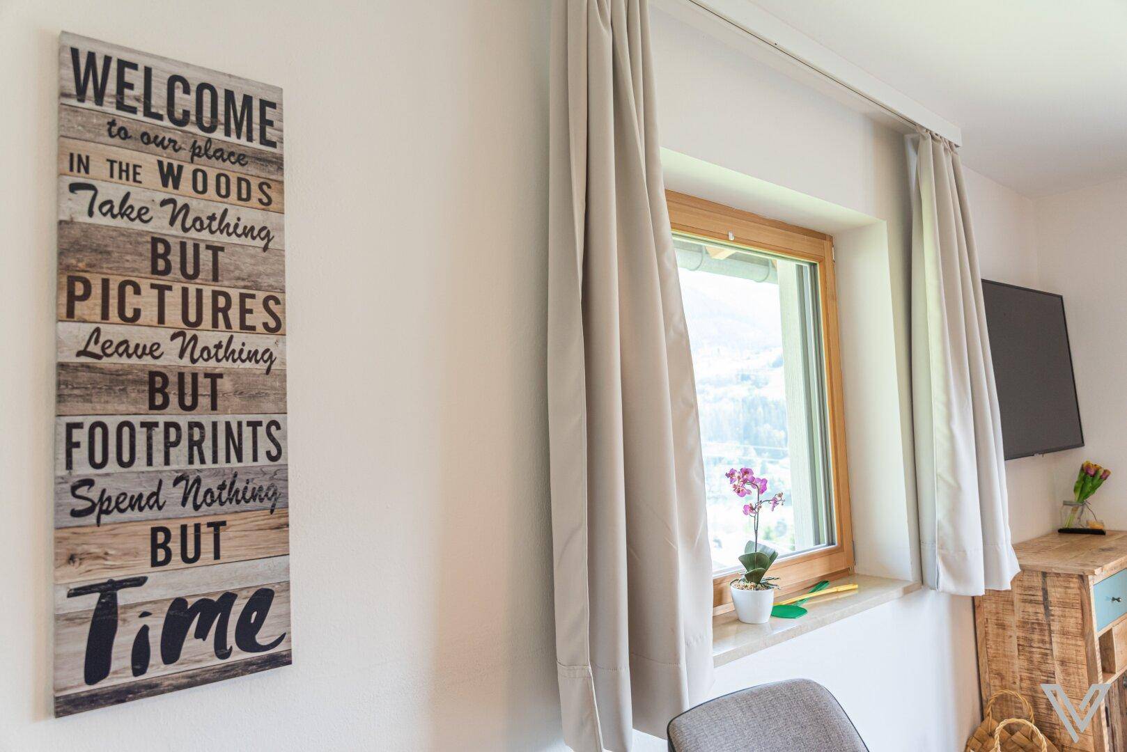 Helles Wohnzimmer mit Fenster, Bergblick und dekorativem Wandbild für eine gemütliche Atmosphäre.
