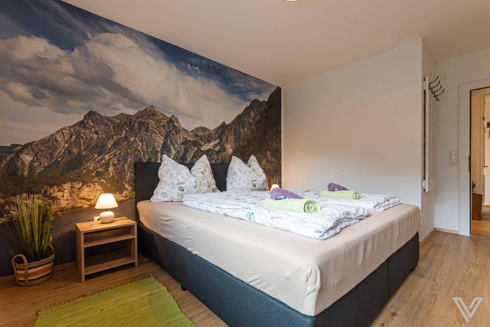 Geräumiges Schlafzimmer mit Doppelbett, Bergblick-Wandbild und praktischen Nachttischen.