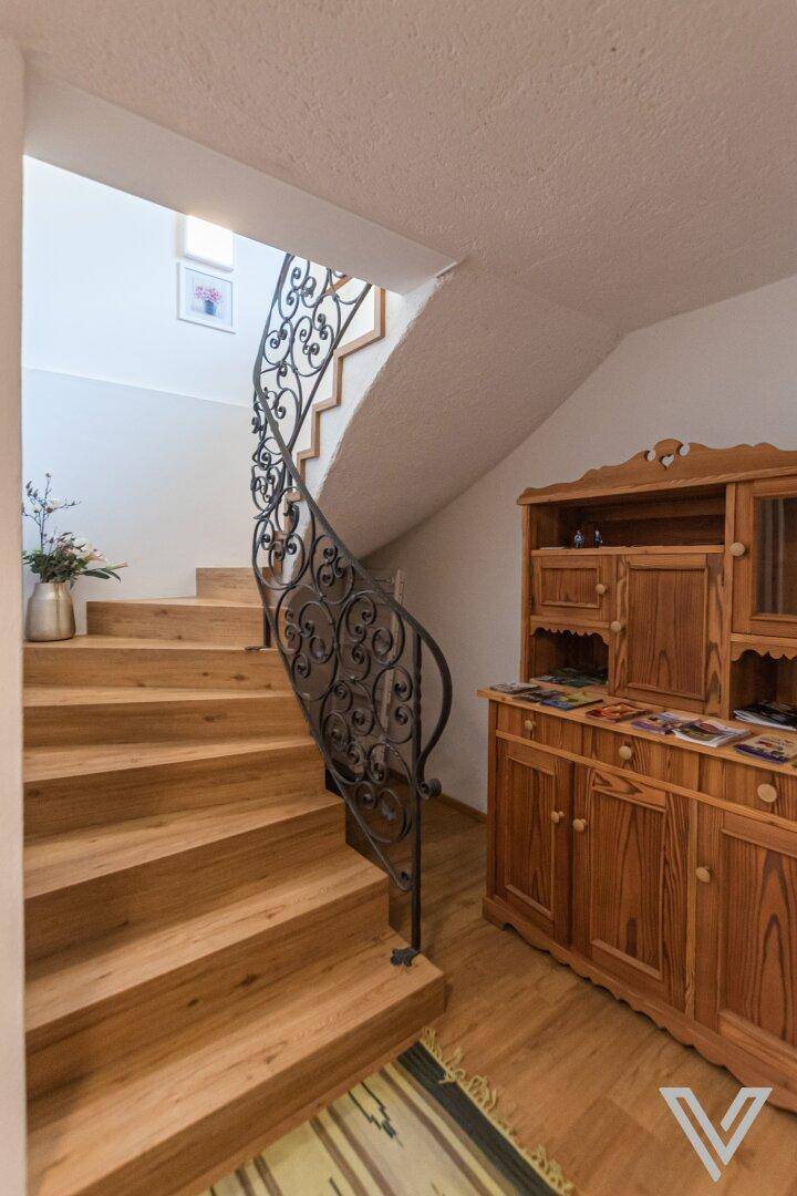 Holztreppe mit schmiedeeisernem Geländer und traditionellem Sideboard im Flurbereich.