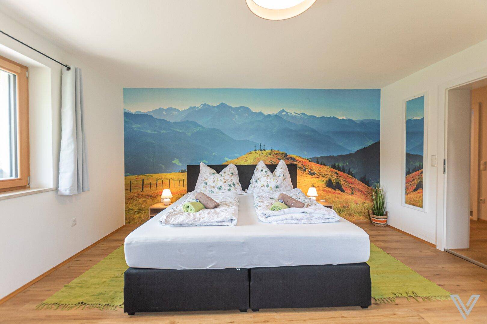 Helles Schlafzimmer mit Doppelbett, Bergblick-Wandbild und Fenster für viel Tageslicht.