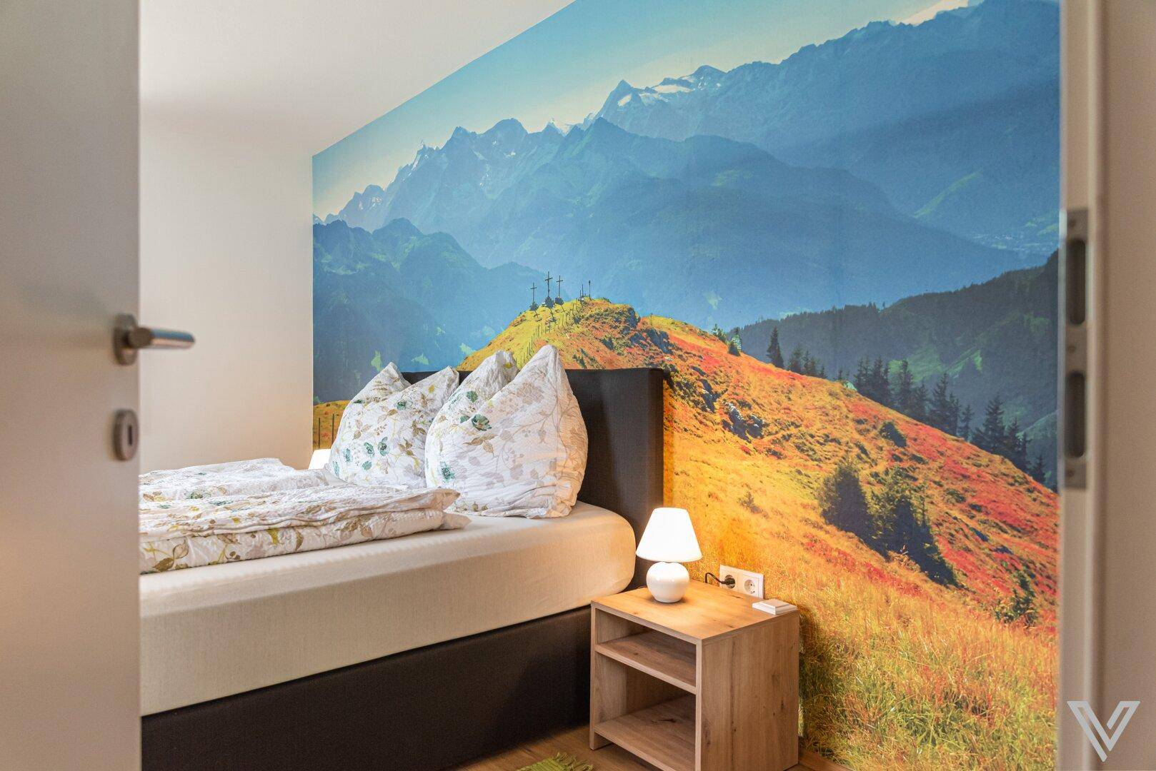 Schlafzimmer mit Einzelbett, farbenfrohem Bergblick-Wandbild und Holzboden.