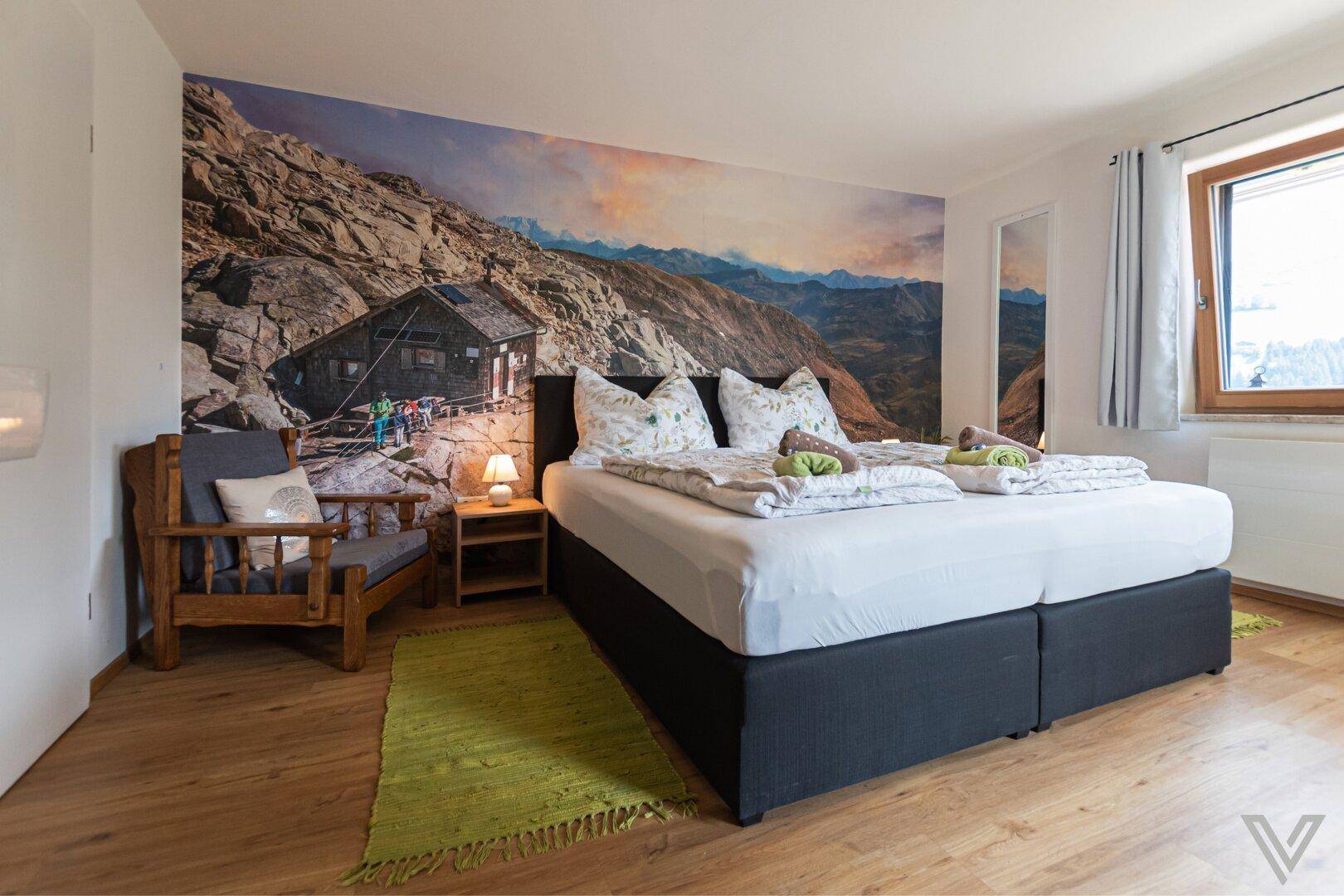 Geräumiges Schlafzimmer mit Doppelbett, Bergblick-Wandbild und Fenster für viel Licht.
