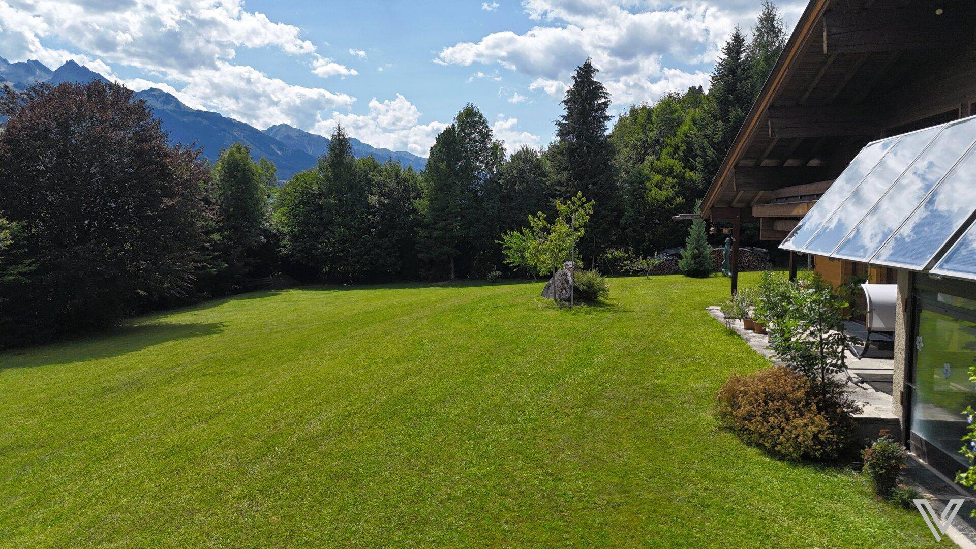 Großer, sonniger Gartenbereich neben dem Haus mit weitem Rasen und alpiner Bergkulisse.