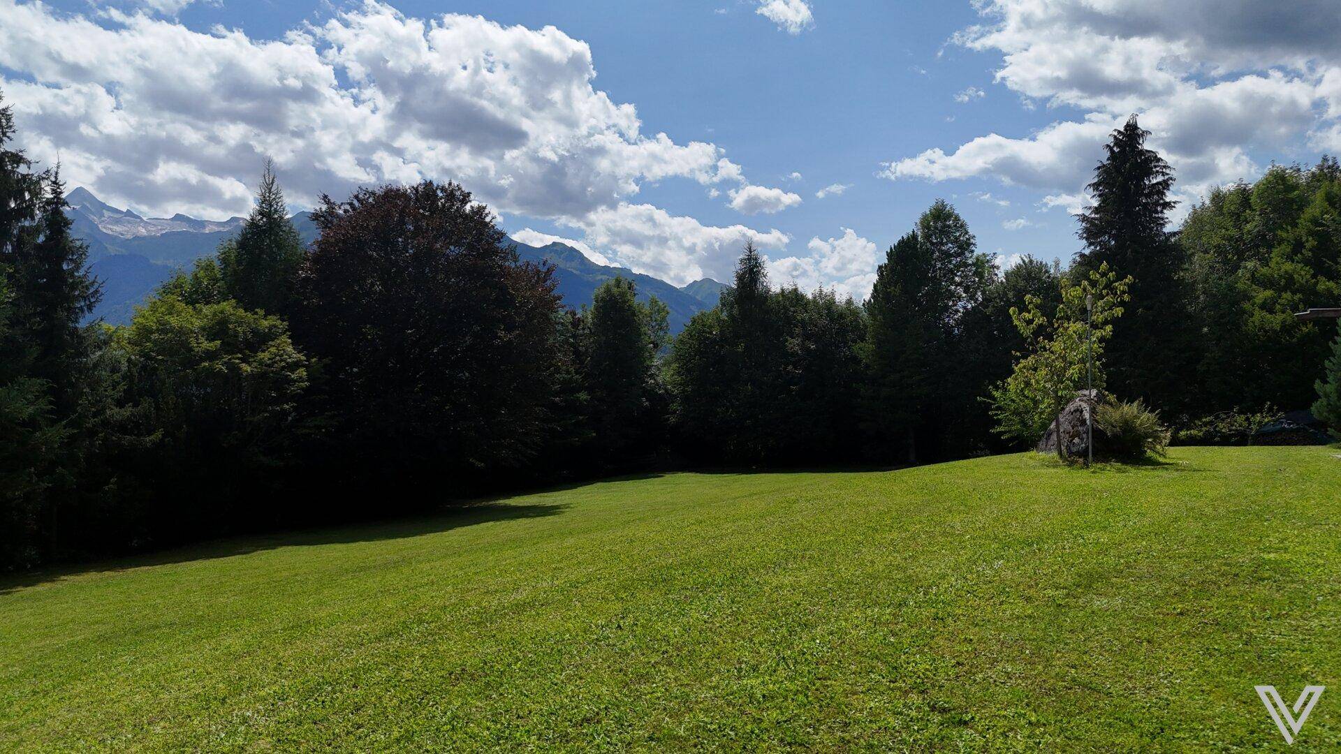 Idyllischer, weitläufiger Garten mit sattgrünem Rasen, umrahmt von Bäumen und majestätischen Bergen.